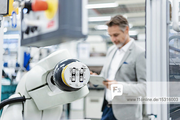Businessman with tablet at assembly robot in a factory