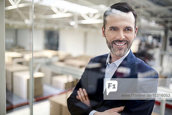 Portrait of a smiling businessman behind glass pane in a factory