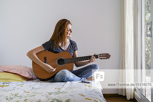 Junge Frau zu Hause chillt im Schlafzimmer und spielt Gitarre