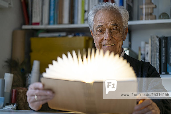 Älterer Mann mit leuchtendem Buch zu Hause