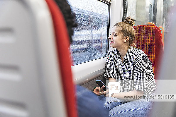 Lächelnde junge Frau  die an einem regnerischen Tag mit ihrem Freund im Zug reist und aus dem Fenster schaut  London  Großbritannien