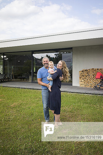 Portrait of happy family of three standing in garden of their home