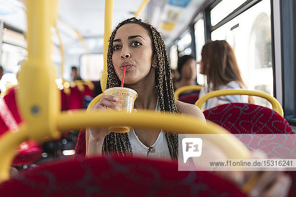 Porträt einer jungen Frau  die im Bus sitzt und Orangensaft trinkt  London  UK
