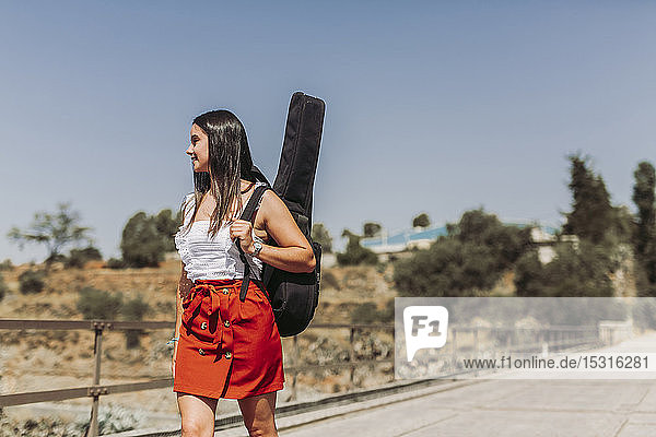 Young woman playing guitar  walking on bridge