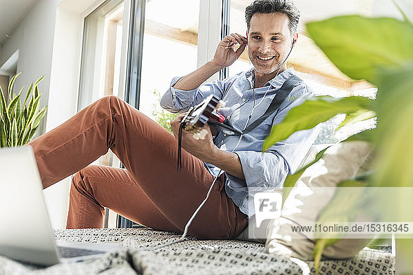 Mature man practising on the guitar using laptop and earphones