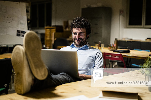 Businessman using laptop in office with feet on desk
