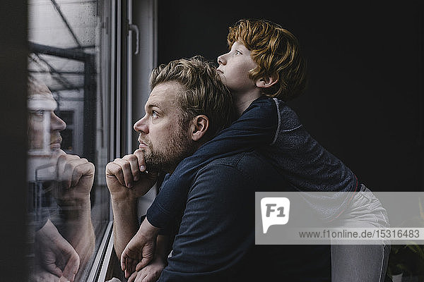 Father and son looking out of window on rainy day