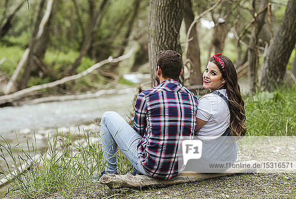 Junges Paar sitzt nebeneinander auf einem Baumstamm