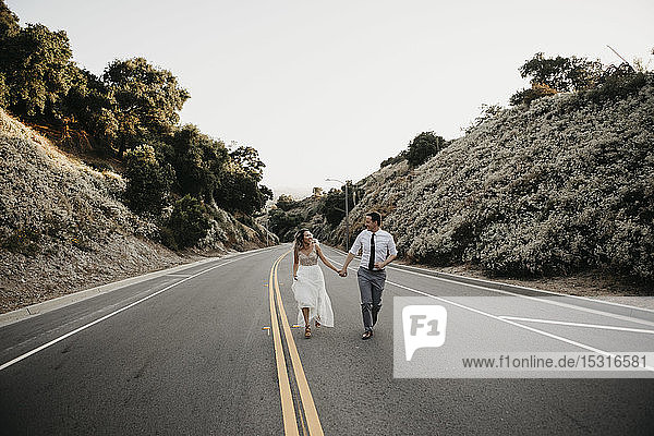 Braut und Bräutigam gehen Hand in Hand auf einer Landstraße