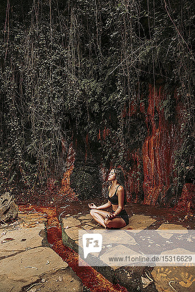 Junge Frau meditiert an einem Wasserfall