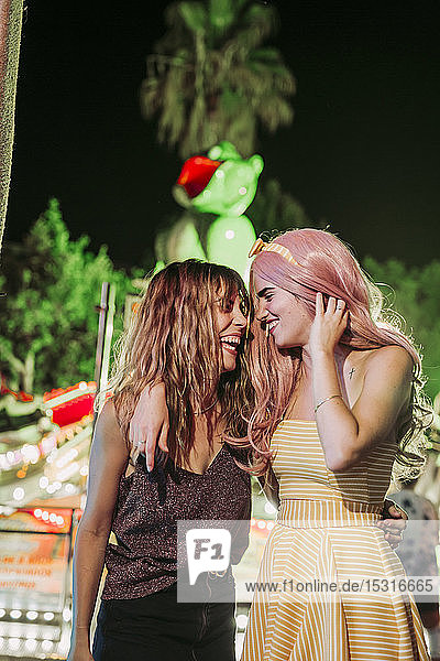 Portrait of two happy young women embracing on a funfair at night