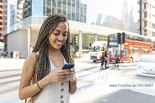 Portrait of smiling young woman in the city looking at cell phone  London  UK