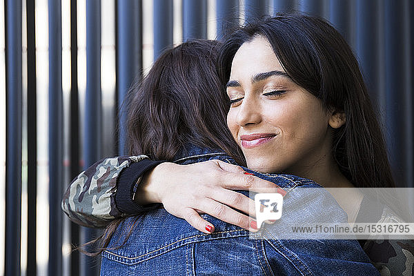 Young female friends with eyes closed embracing together at wall