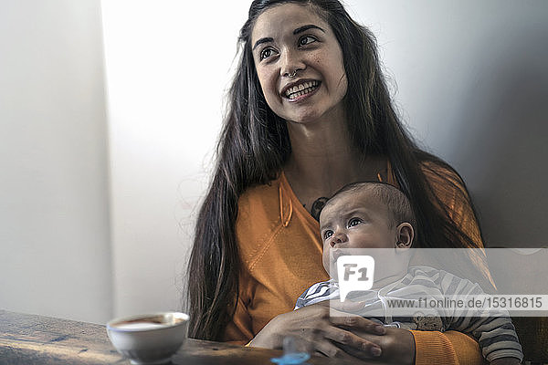 Glückliche Mutter mit Baby zu Hause am Holztisch sitzend