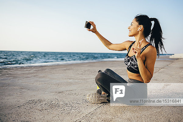 Frau mit Smartphone und Selbstbedienung  auf einem Pier sitzend