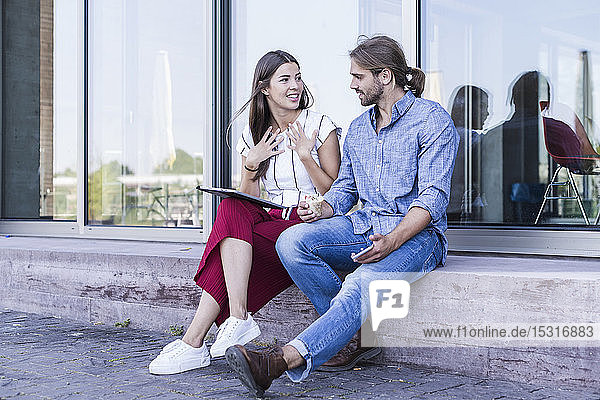Junges Paar sitzt auf der Fensterbank eines Gebäudes und benutzt ein Tablett