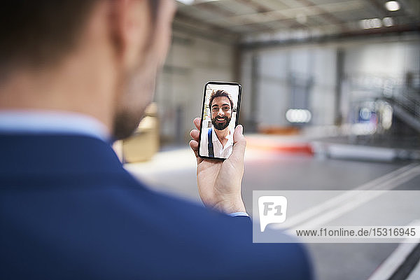 Close-up of businessman using smartphone chatting with colleague in factory