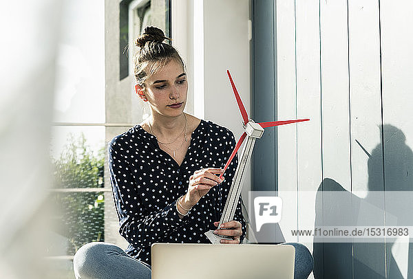 Junge Frau zu Hause hält Modell einer Windkraftanlage
