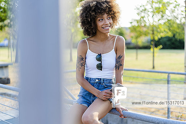 Porträt einer tätowierten jungen Frau mit Smartphone im Sommer
