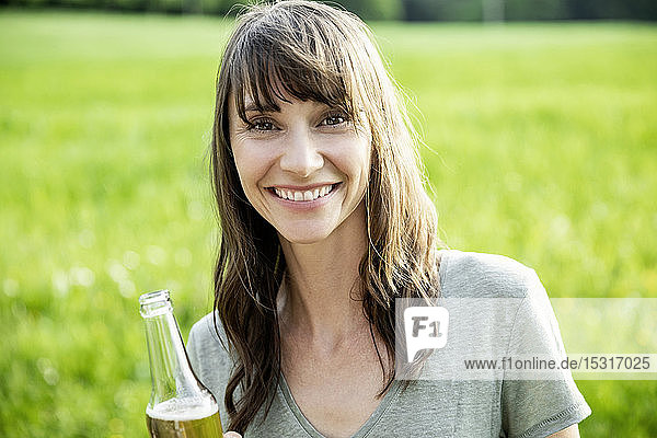 Porträt einer lächelnden brünetten Frau mit einer Bierflasche im Freien