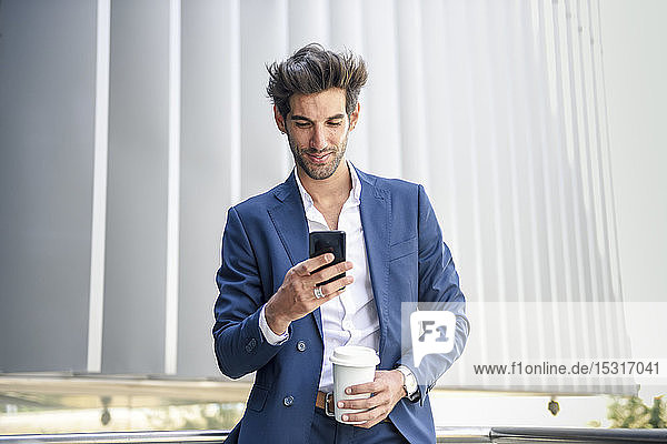 Smiling businessman using smartphone taking a coffee break outdoors