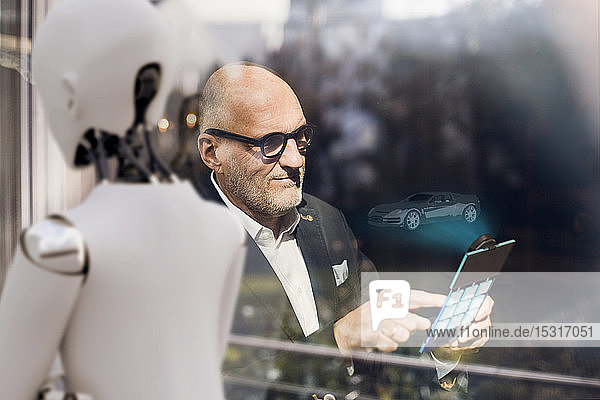 Leitender Geschäftsmann mit digitalem Tablet  auf der Suche nach computergesteuerten Autos