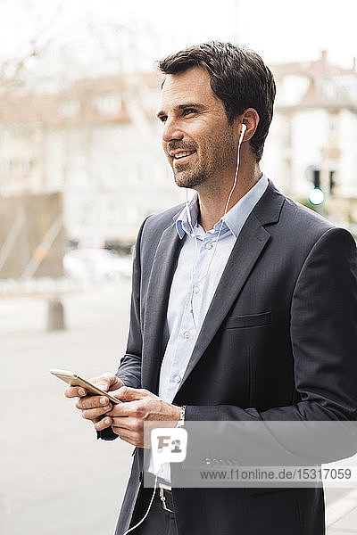 Porträt eines Geschäftsmannes mit Mobiltelefon und Ohrstöpseln in der Stadt