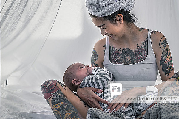 Glücklich tätowierte junge Frau mit ihrem Baby im Himmelbett