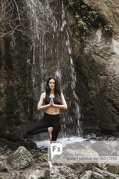 Woman practising yoga at waterfall tree position