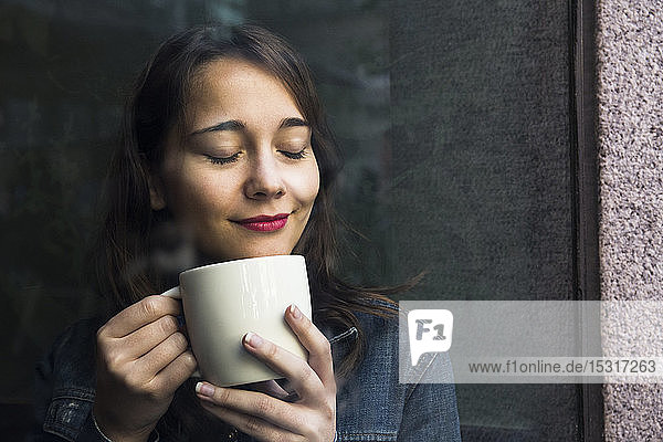 Young woman in cafe with cup of coffee and closed eyes