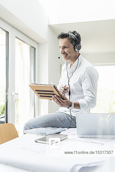 Businessman in bright office having conference call using headset and digital tablet