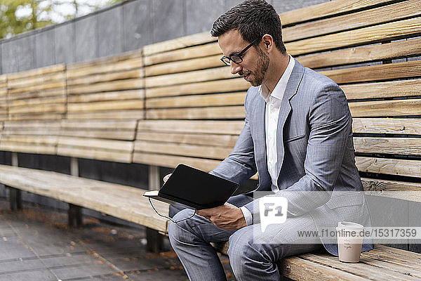 Geschäftsmann sitzt auf einer Holzbank in der Stadt und schreibt in ein Notizbuch