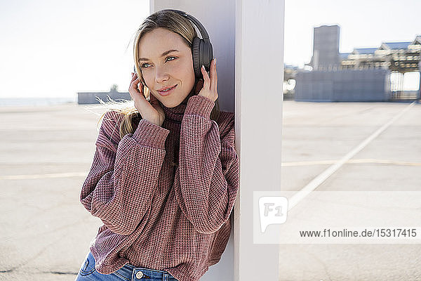 Portrait of smiling young woman listening music with wireless headphones  Barcelona  Spain