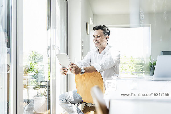 Mature man sitting on chair backwards using digital tablet