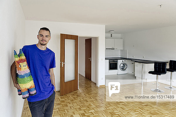 Junger Mann steht in einer leeren Wohnung und hält eine Pinata