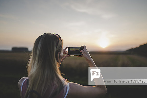 Woman taking a photo of sunset with her smartphone