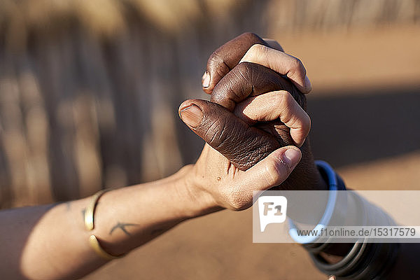 Traditionelle Muhacaona-Frau und weiße Frau halten Händchen  Oncocua  Angola
