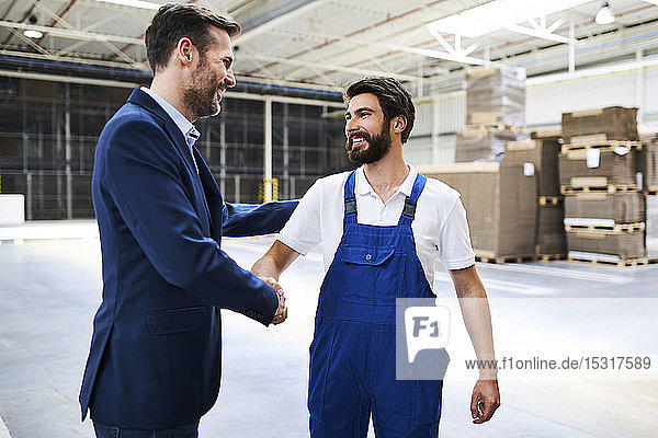 Businessman and worker shaking hands in a factory