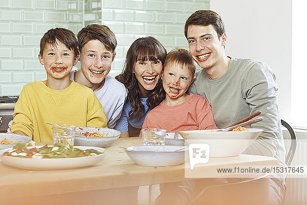 Porträt von Mutter und Söhnen beim Mittagessen  mit Gesichtern voller Tomatensauce