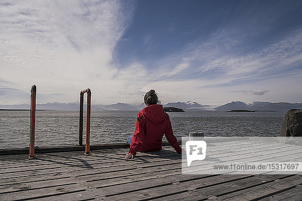 Junge Frau sitzt auf einem Steg und schaut auf das Meer  Südost-Island