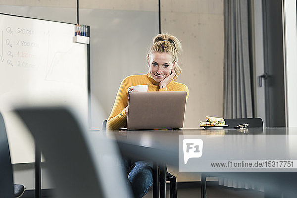 Lässige Geschäftsfrau sitzt am Tisch im Konferenzraum und schaut auf den Laptop