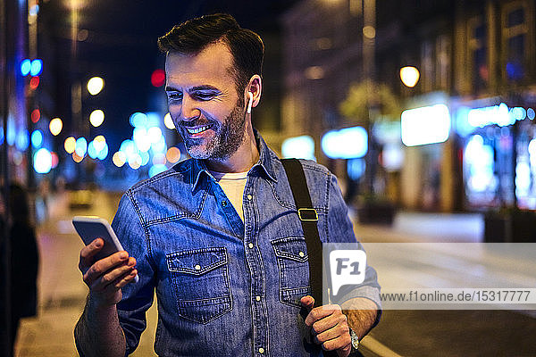 Mann mit drahtlosen Kopfhörern mit Smartphone in der Stadt bei Nacht