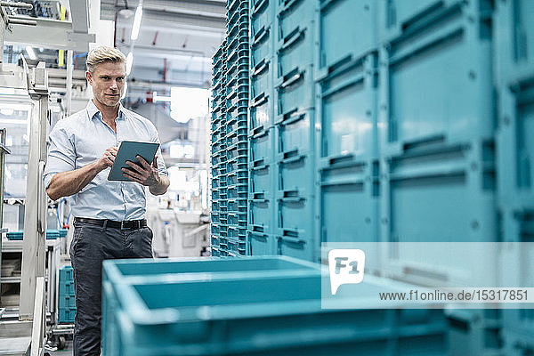 Businessman using tablet in a factory hall with boxes