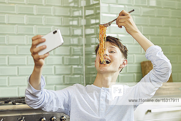 Lachender Junge nimmt Smartphone-Selfie  isst Spaghetti