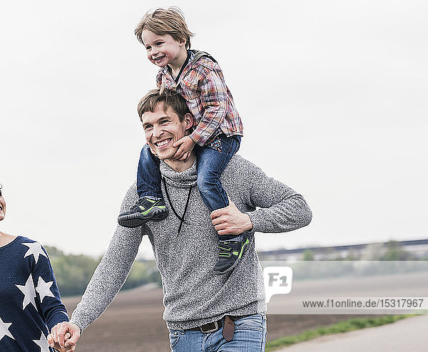 Glückliche Familie beim gemeinsamen Spaziergang neben den Feldern  Vater trägt Sohn huckepack