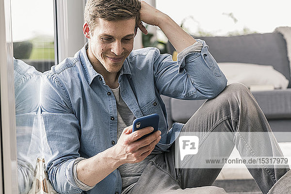Mid adult man sitting by window  using smartphone