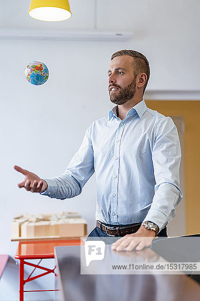 Businessman throwing up miniature globe in office
