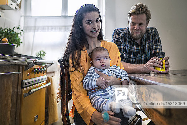 Porträt einer Familie mit einem Baby  das zu Hause am Küchentisch sitzt