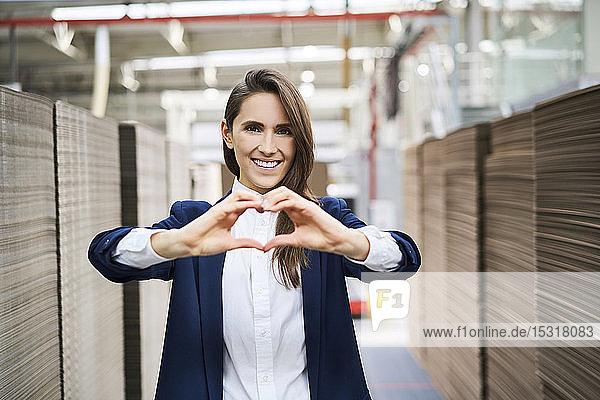 Porträt einer glücklichen Geschäftsfrau im Fabriklager  die mit ihren Händen ein Herz formt