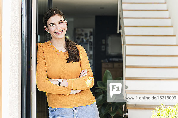 Portrait of smiling young woman leaning against terrace door